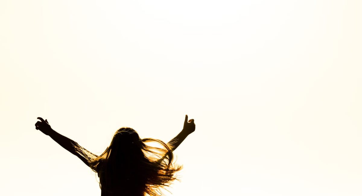 Backlit silhouette of a woman with arms up, capturing freedom and joy in a minimalist setting.