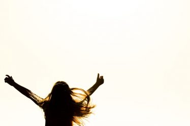 Backlit silhouette of a woman with arms up, capturing freedom and joy in a minimalist setting.