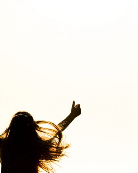 Backlit silhouette of a woman with arms up, capturing freedom and joy in a minimalist setting.