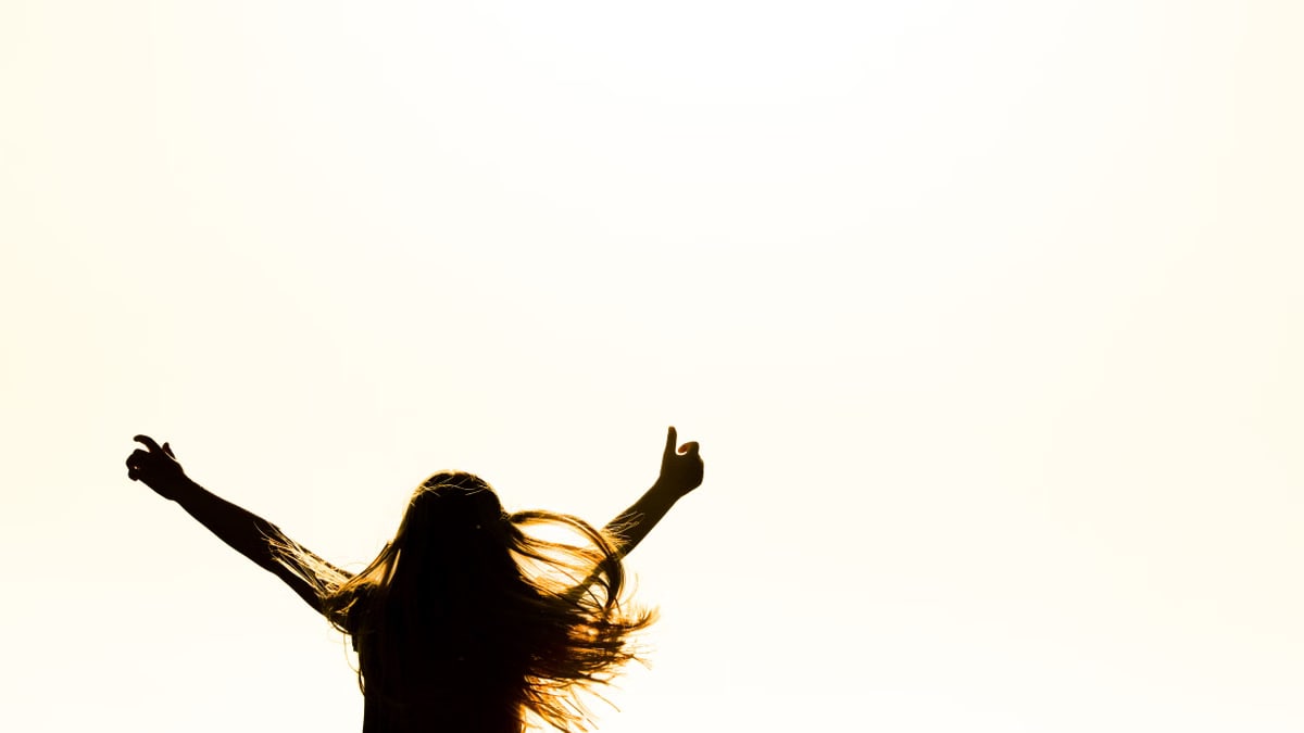 Backlit silhouette of a woman with arms up, capturing freedom and joy in a minimalist setting.