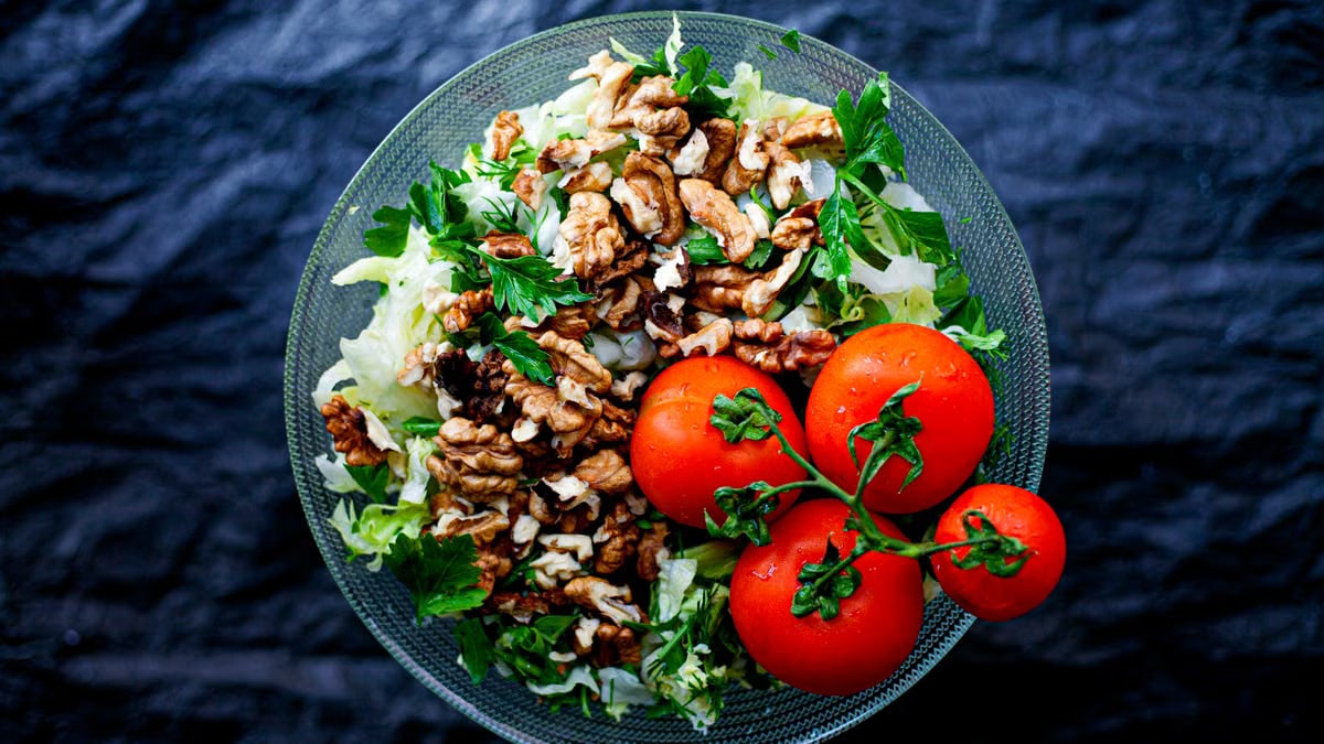 Top view of a fresh mixed salad with walnuts and tomatoes in a glass bowl, emphasizing healthy eating.